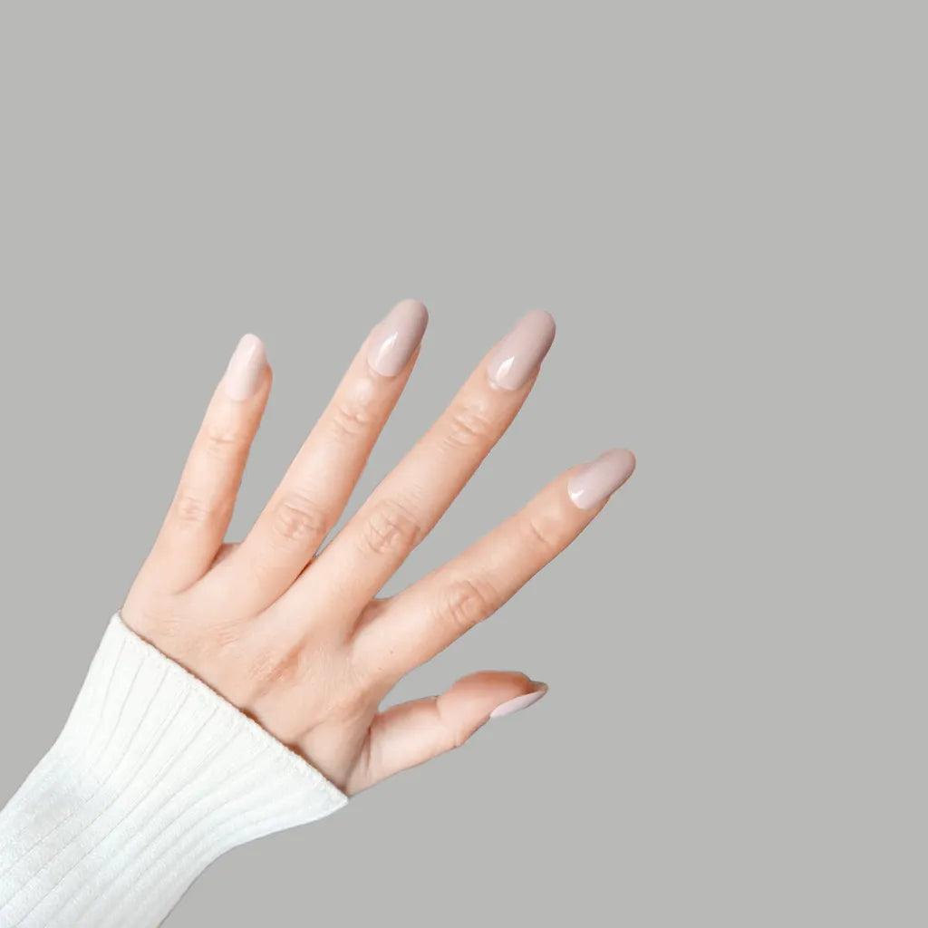 Fingers up pose showing de blinkie Bare Elegance soft pastel pink nude high gloss press-on nails in short oval shape against grey background with white ribbed knit sleeve