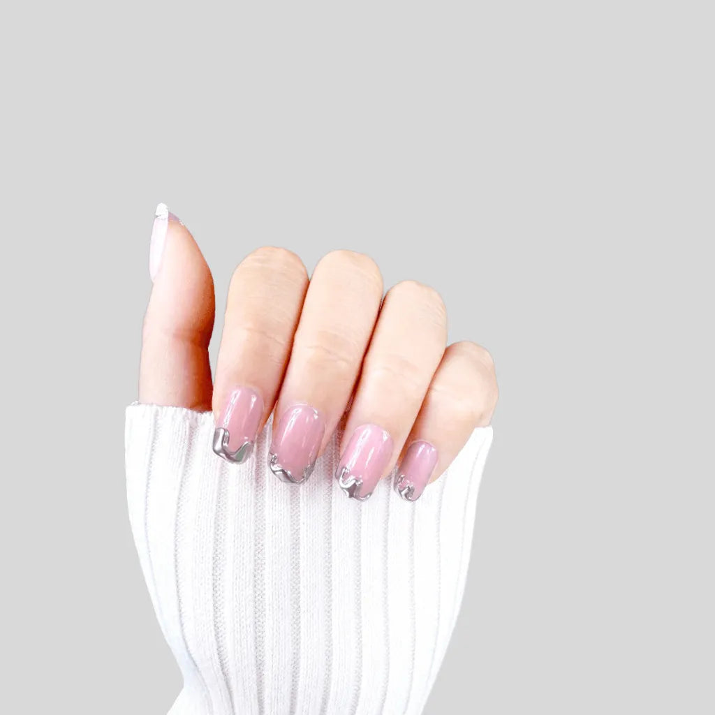 Claw pose showing de blinkie Chrome Whispers blush pink with sculptural silver chrome tips in short square shape against grey background with white ribbed knit sleeve