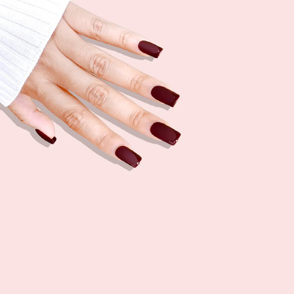 Fingers down pose showing de blinkie Velvet Bordeaux dark burgundy velvet matte press-on nails in medium square shape against pink background with white ribbed knit sleeve