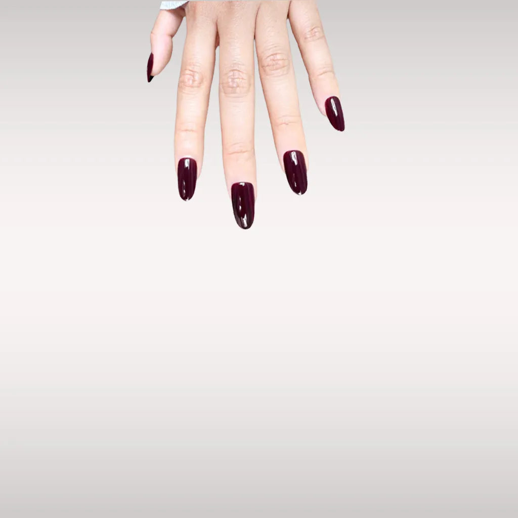 Fingers down pose showing de blinkie Velvet Noir dark bordeaux high gloss press-on nails in short oval shape against off-white background with white ribbed knit sleeve